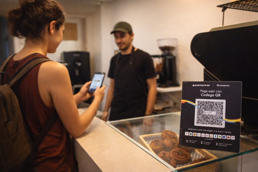 Traveler using a smartphone to pay with a QR code at a local coffee shop in Latin America, illustrating digital payment methods for tourists.